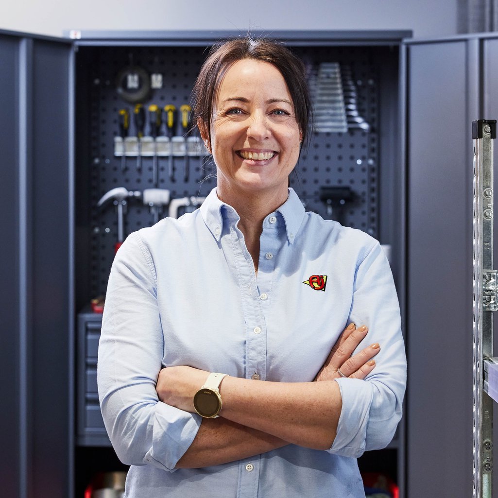 Zaposlena ženska stoji v delavnici pred omaro za orodje