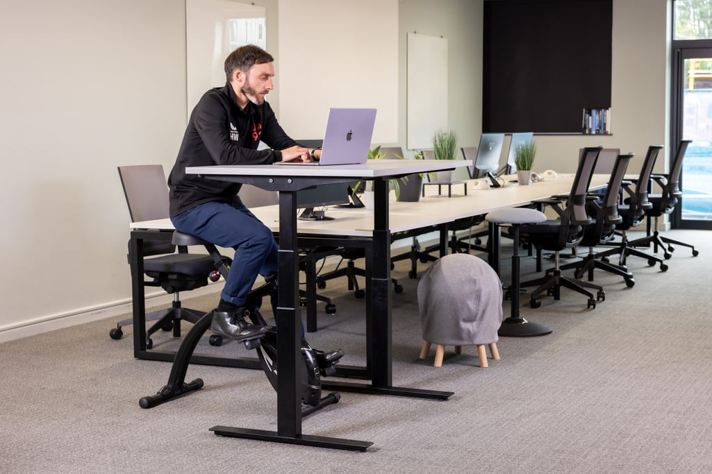 Man working at a standing desk while using an under-desk exercise bike in a modern office setting.