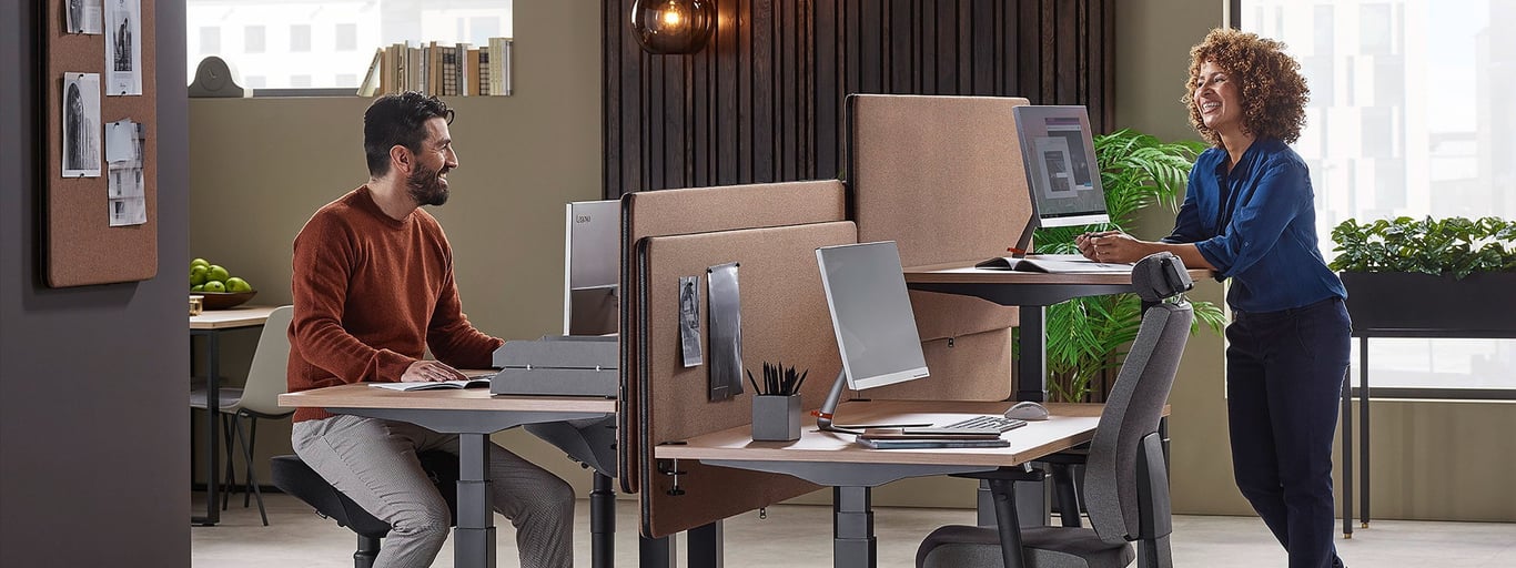 Two work colleagues smiling and engaged on a discussion while reviewing documents on their computer