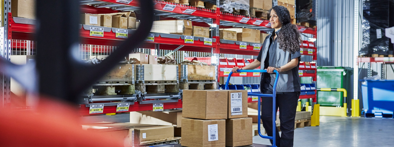 A woman pushing a goods trolley in a warehouse setting