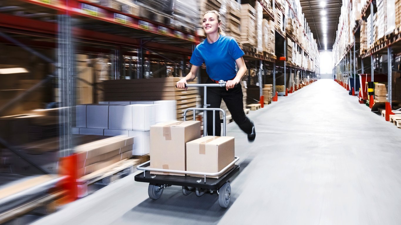 Person going at speed while using a platform trolley in warehouse aisle