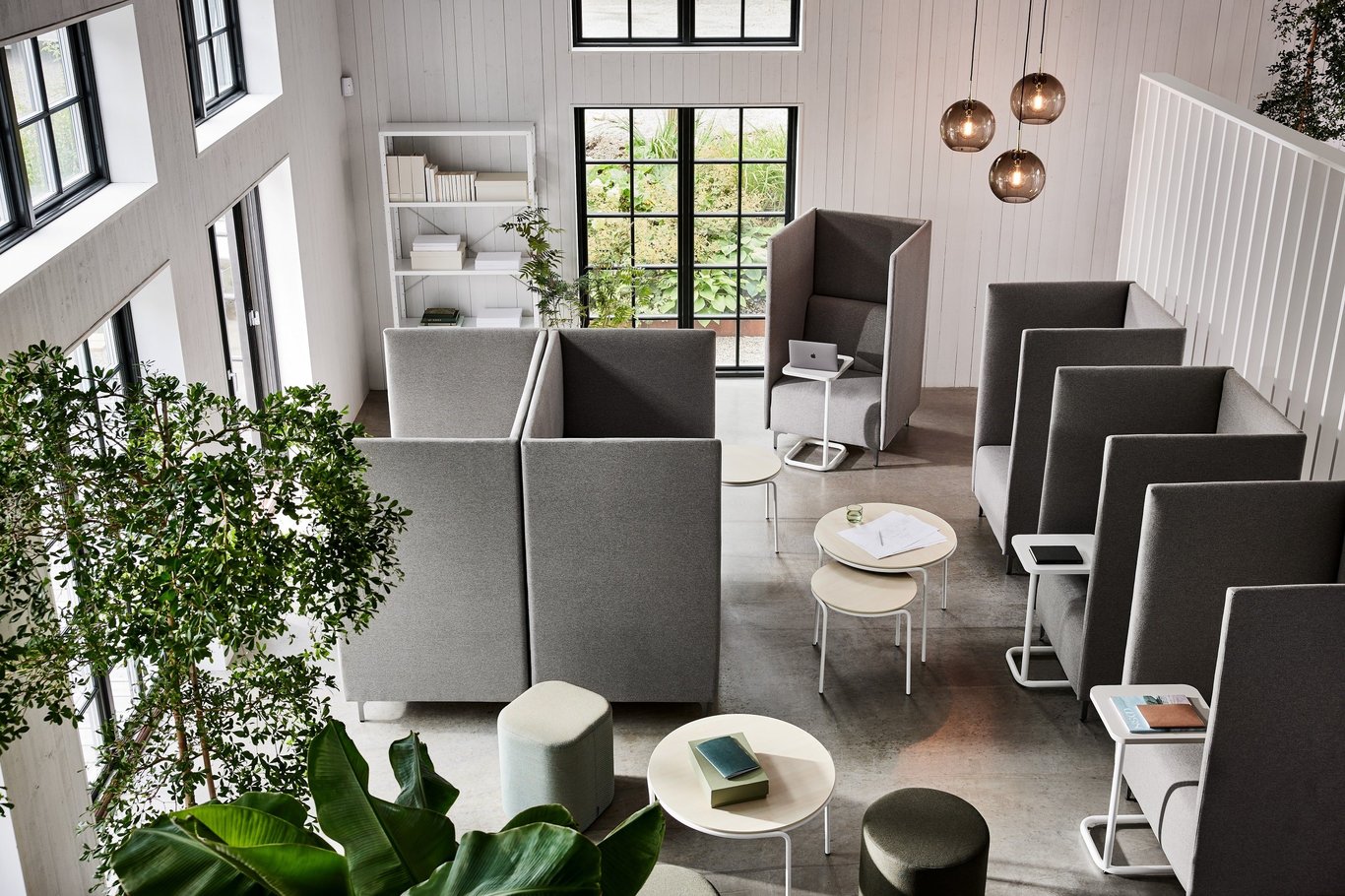 Pogled iz ptičje perspektive na prilagodljiv odprt pisarniški prostor s kavči z visokimi stranicami in mizami, ločenimi z zasloni