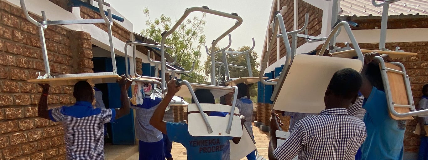 School children in an African village carrying chairs