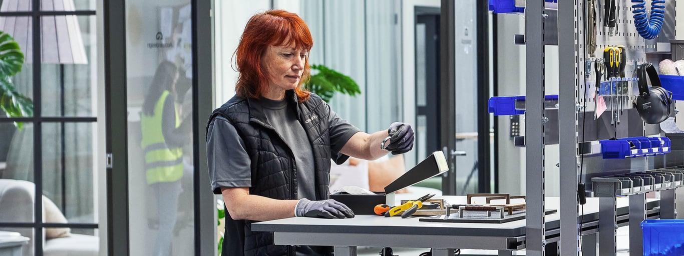 Person som arbetar vid en höj- och sänkbar arbetsbänk i en verkstadsmiljö. 