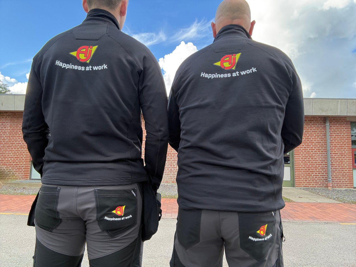 Montører fra AJ Produkter står med ryggen til. De har et AJ Produkter logo på ryggen af arbejdstøjet.