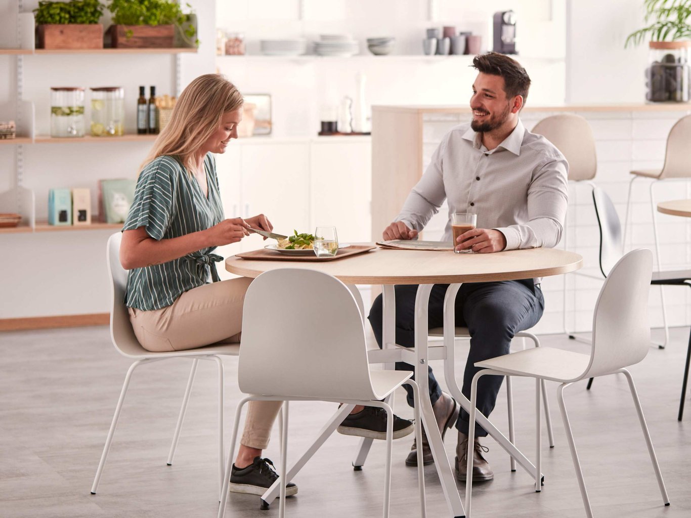 To personer sidder og spiser og drikker kaffe i en lys kantine