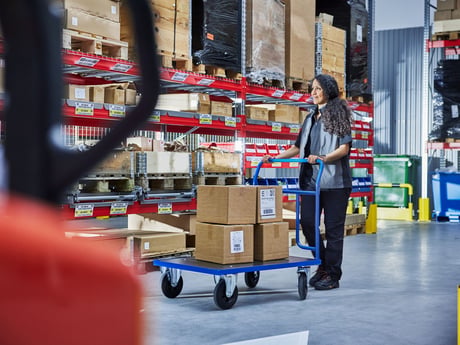 A woman pushing a goods trolley in a warehouse setting