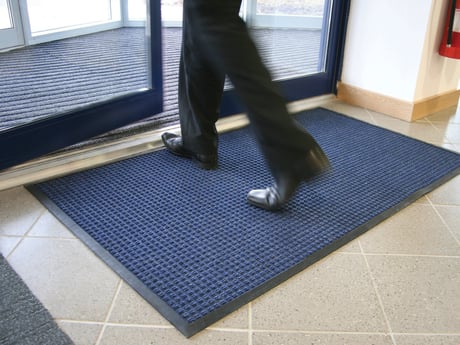 a close-up of someone stepping onto a blue textured doormat inside a building