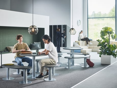 Two young adults engaged in conversation in a brightly lit, modern, open-plan space that can be a co-working area or study space