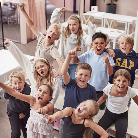 Bērnu grupa klasē priecīgi paceļ rokas un sauc.