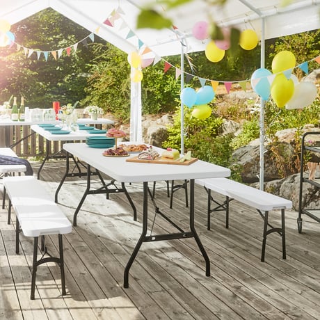 Several long white folding tables and benches arranged neatly under a transparent canopy, which serves as both a shelter and a decorative frame for the party