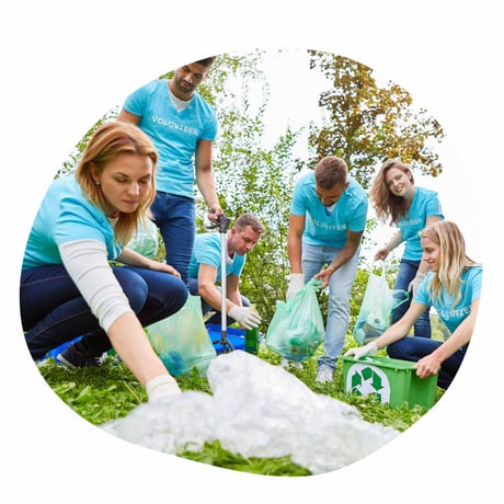 Kolleger iført blå t-shirts er på teambuilding udendørs, hvor de gør noget godt for miljøet