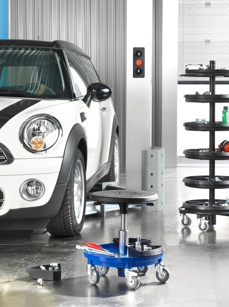 a close up caption of a wheeled stool beside a car in a car garage