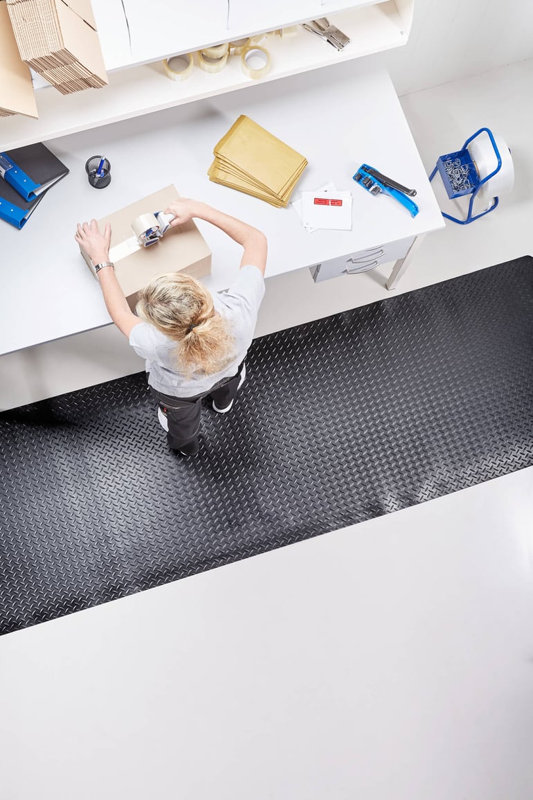 warehouse person using a packing table and standing on an anti fatigue mat