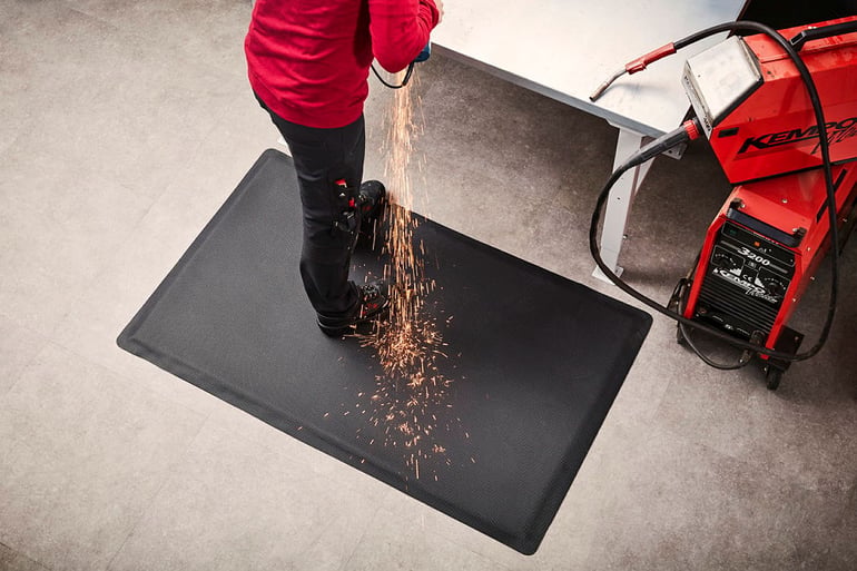 A person welding on an anti-fatigue welding mat that withstands sparks and hot metal chips