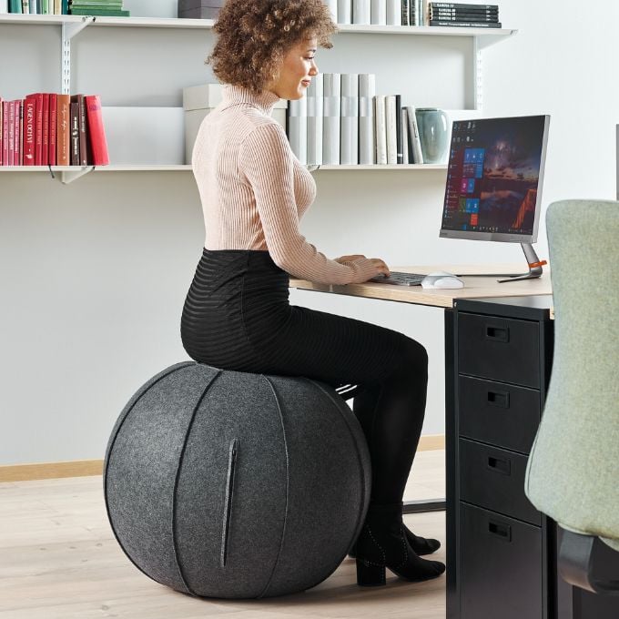 a woman sitting on a pilates balance ball while she works at her desktop