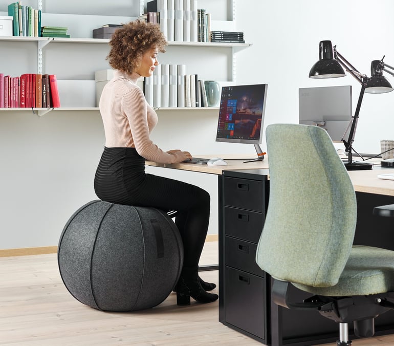 an office employee working at her desk sitting on a pilates balance ball
