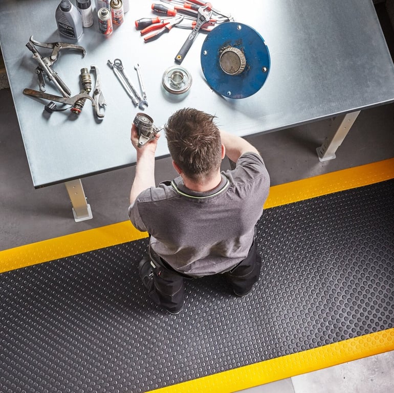 a man working assembling a product in front of a desk full of tools and standing on an anti-fatigue mat