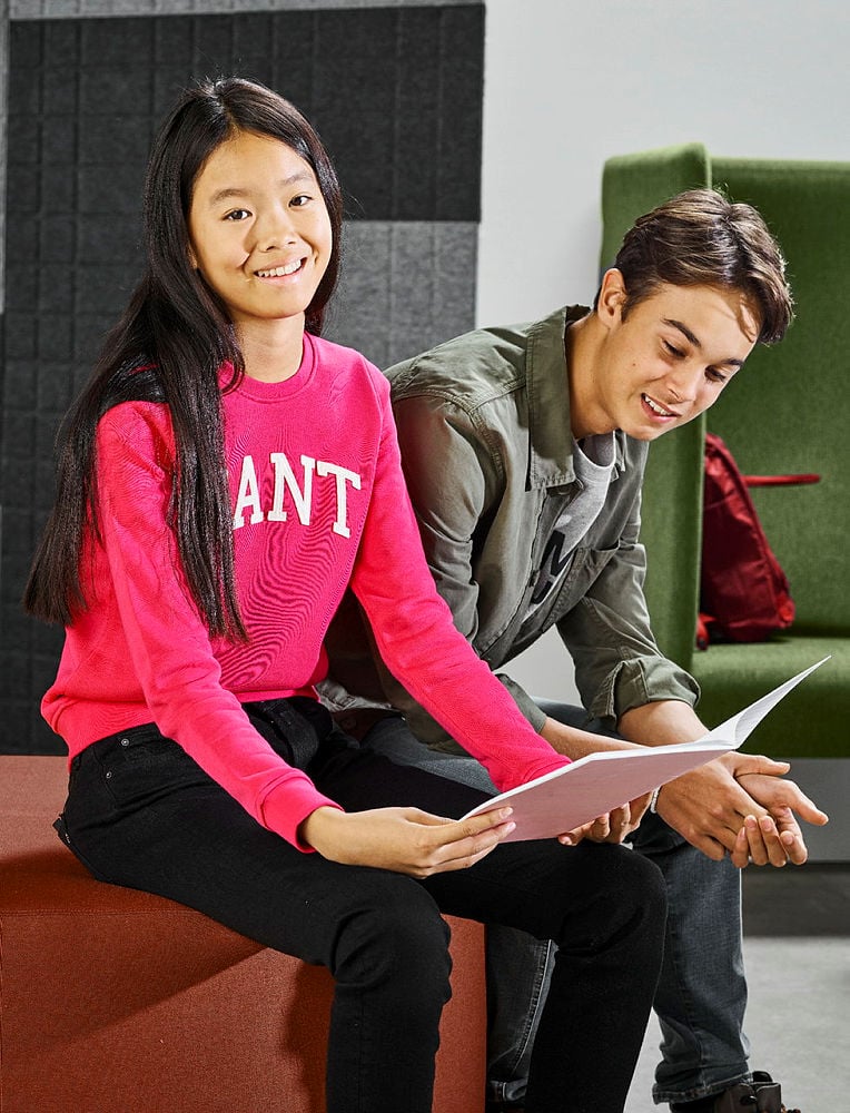 A young girl and boy sitting together in the school breakout room looking at a book.