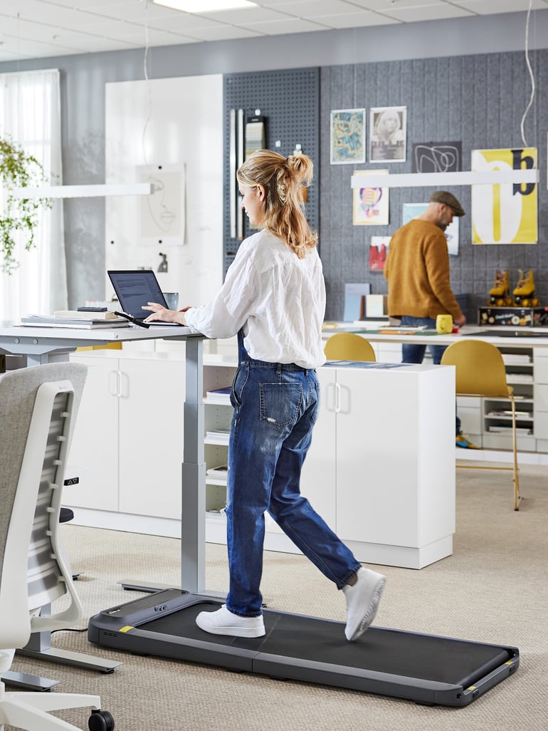 A person walks on a treadmill while working at a height adjustable desk in an office