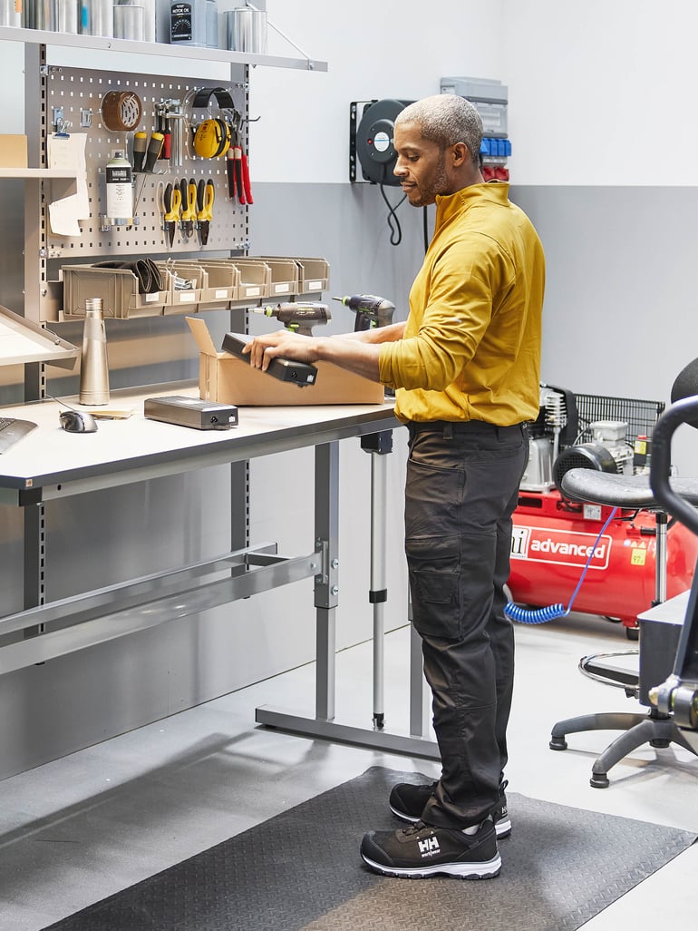 Verkstadsarbetare lutar sig mot arbetsbänk av stål