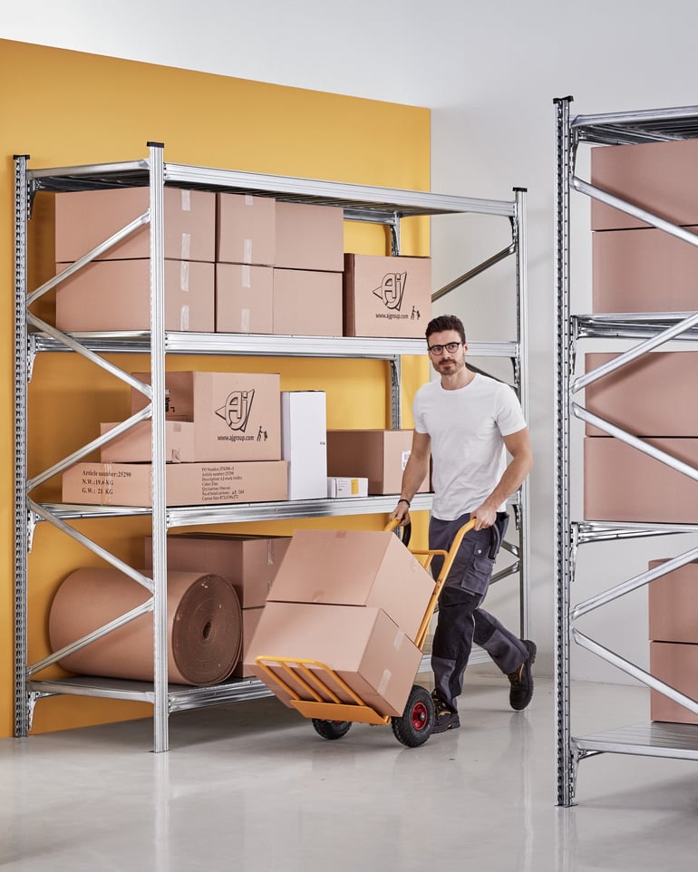 A warehouse worker transports boxes on a warehouse trolley.