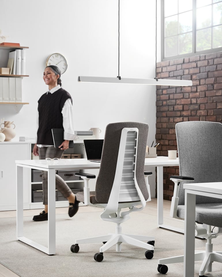 Smiling woman in a bright office with hanging lighting over the desk.