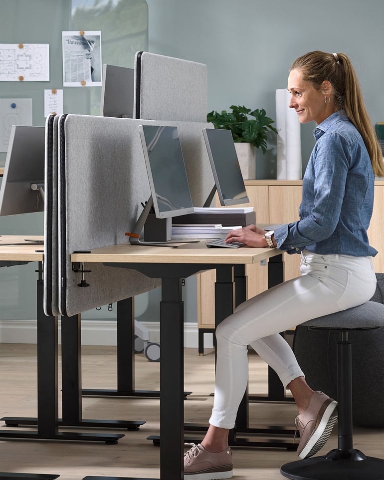 a woman sits at a desk equipped with desktop screens and performs computer work