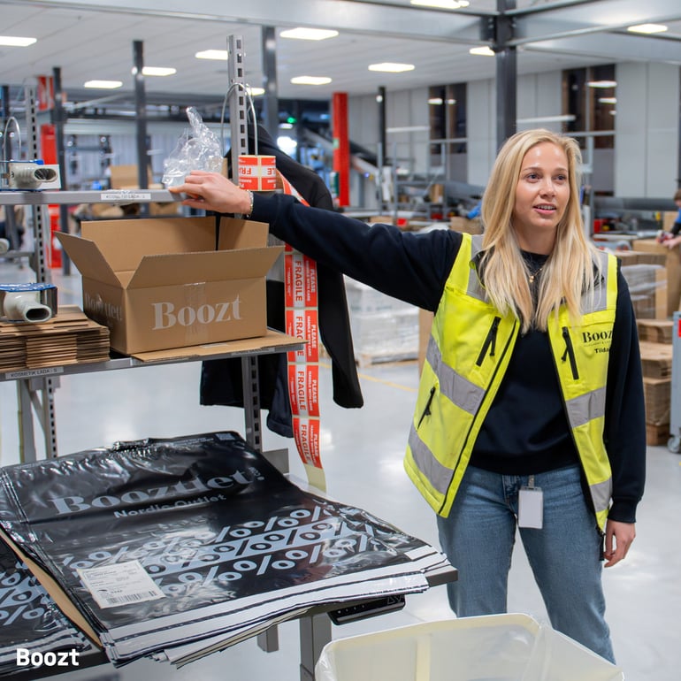 a woman wearing a high-visibility vest working on a packing station at a warehouse