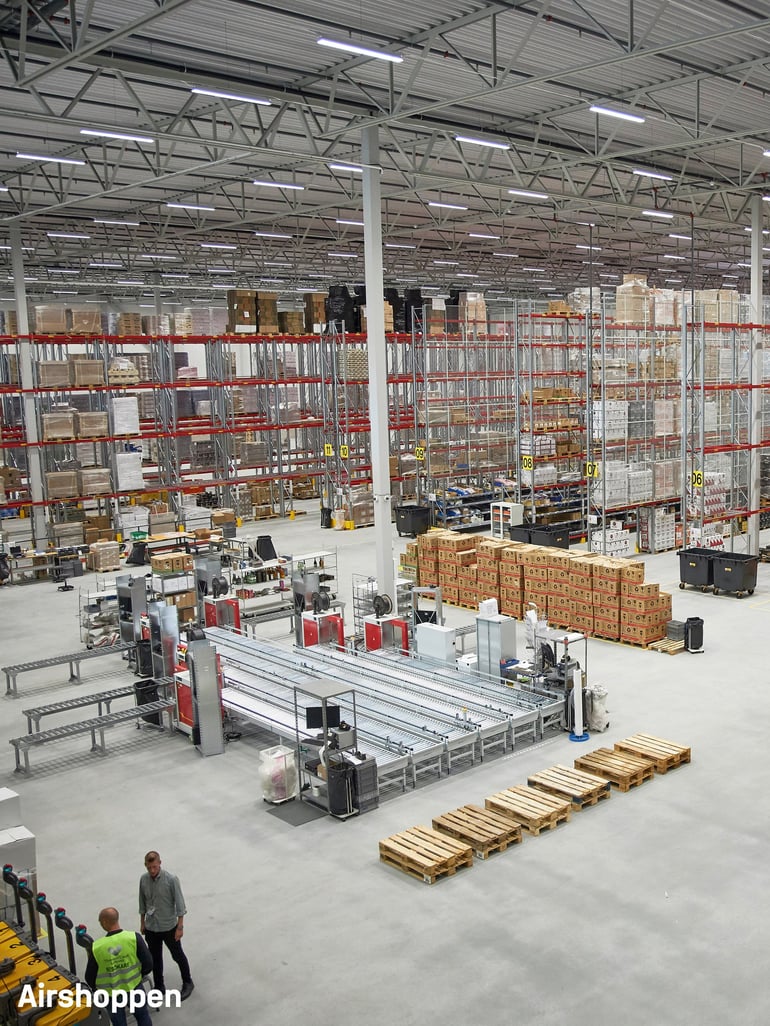 modern warehouse with high ceilings, extensive shelving units stocked with boxes and pallets and a conveyor belt system for efficient product movement