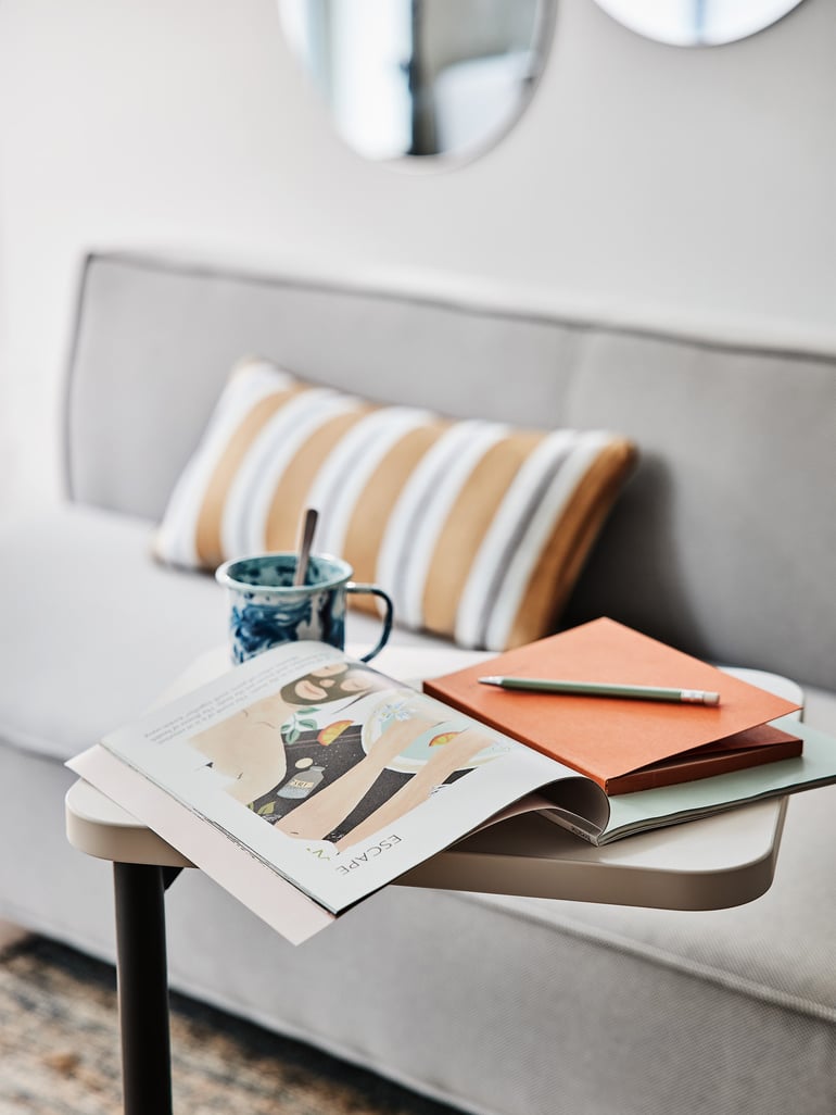 Et magasin og en kaffekop står på et flytbart bord foran en loungesofa