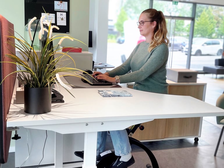 Eine Frau sitzt an einem Desk Bike und arbeitet an ihrem Schreibtisch