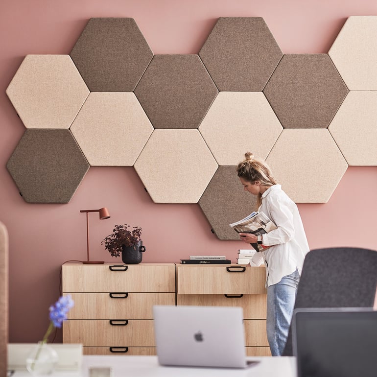 an office setup with oak drawer cabinets and hexagon shaped acoustic wall panels in mute tones