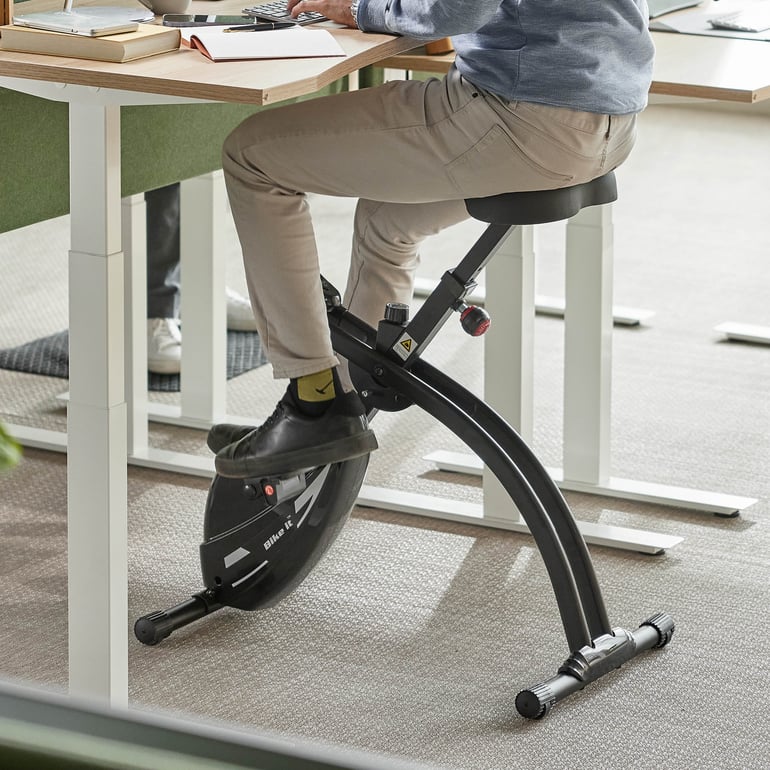 En person trampar på en skrivbordscykel medan man sitter vid ett skrivbord i en kontorsmiljö.