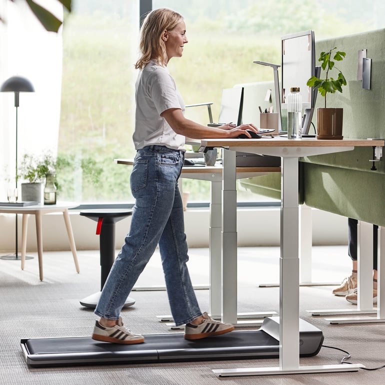En person går på ett skrivbordslöpband i en kontorsmiljö och främjar aktivt arbete.
