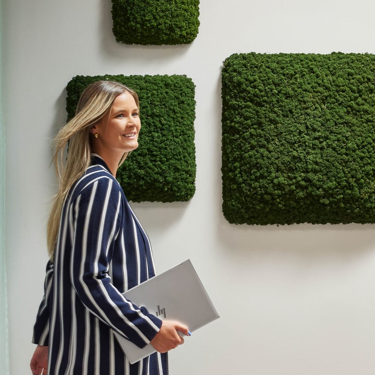 En person står framför en grön akustikväggpanel med levande växter.