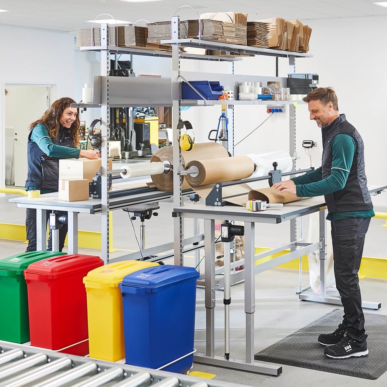 Två personer arbetar i fabriksmiljö, fokuserade på maskiner och uppgifter.