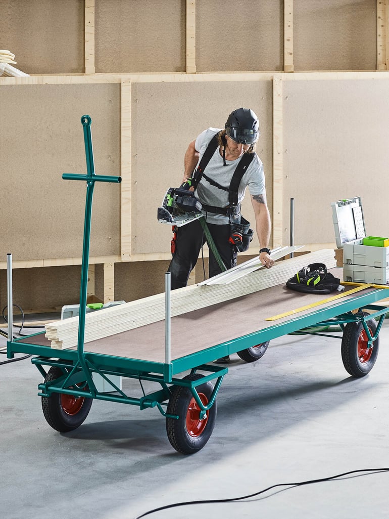 En person som bär hjälm står bredvid en vändskiva i en lagermiljö.