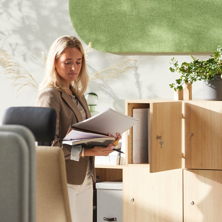 Person som ler när han står nära en bokhylla i en kontorsmiljö med låsbar personlig förvaring.