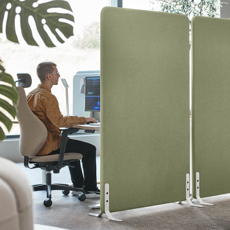 En person sitter vid ett skrivbord och använder en golvskärm för avskildhet.