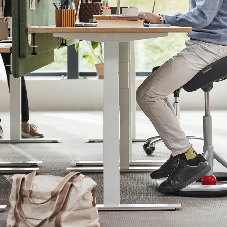 En person sitter vid ett höj- och sänkbart skrivbord och arbetar med en bärbar dator.