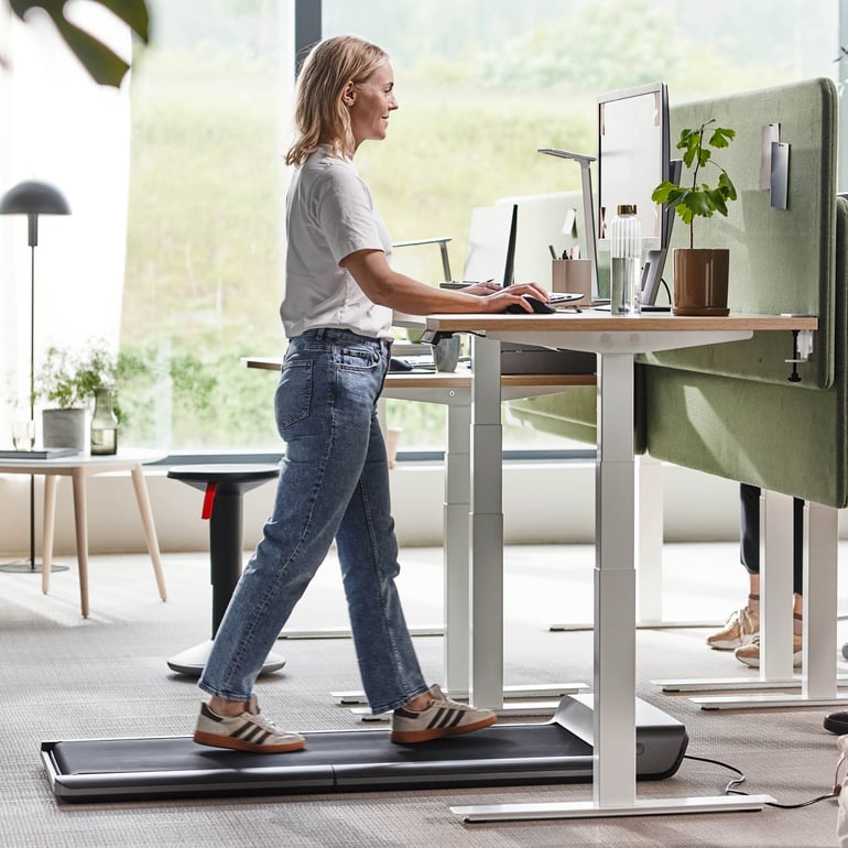 En person som går på ett löpband på ett skrivbord i en kontorsmiljö och främjar aktivt arbete.