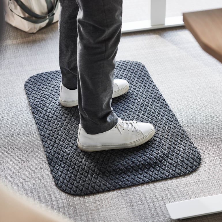 En person står på en matta inomhus och visar upp skor på en plan golvyta.