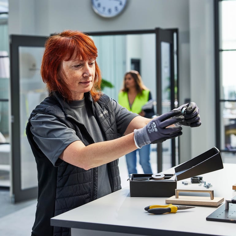 Person som står vid en höj- och sänkbar arbetsbänk i en verkstadsmiljö.