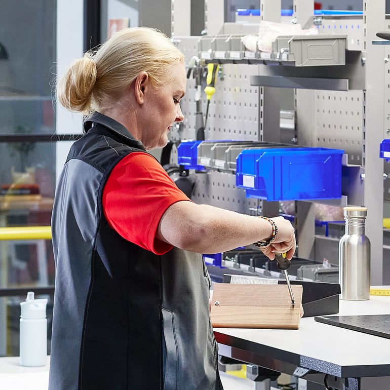 Person som arbetar i en verkstad, fokuserad på en träbit med ett verktyg i närheten.