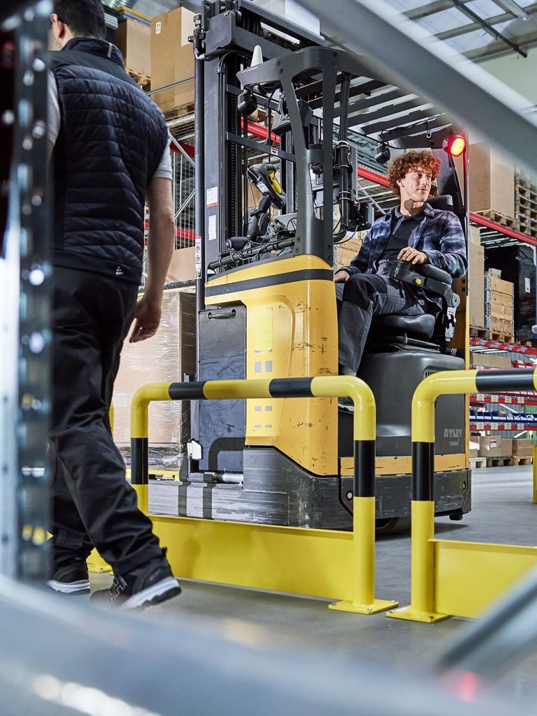 a person operating a pallet stacker beside a collision protection barrier