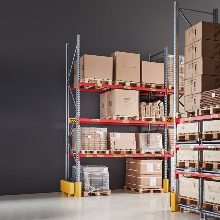 well-organized, industrial storage and distribution area with metal racking systems, with red supports and gray metal beams holding numerous carboard boxes and wooden pallets