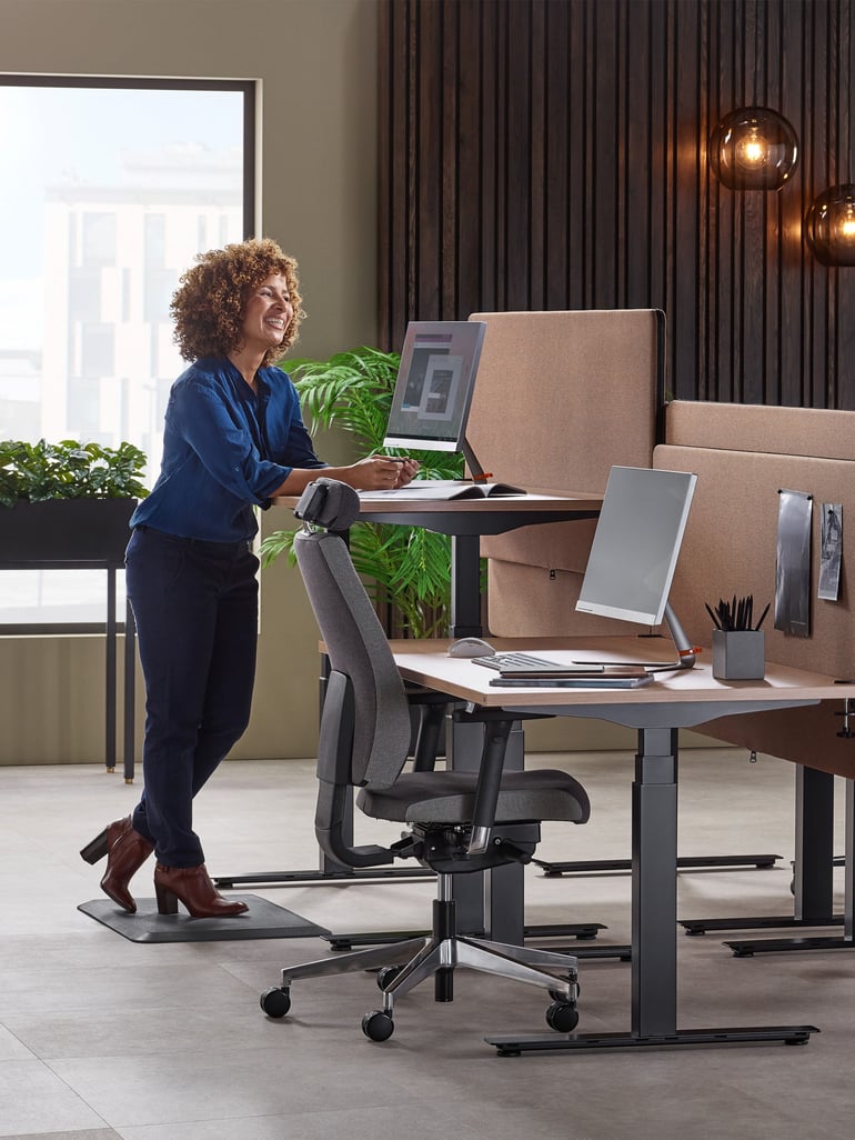 Een vrouw staat op een werkmat aan een in hoogte verstelbaar bureau