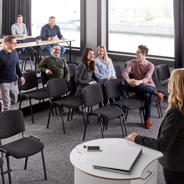 Cheerful employees gather for a big meeting in a room furnished with stackable chairs