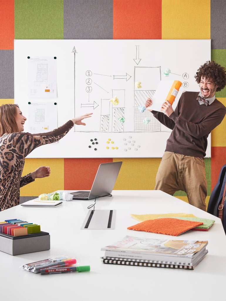 Two people joking with each other in front of a whiteboard in a meeting room